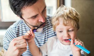 dad brushes teeth with young son